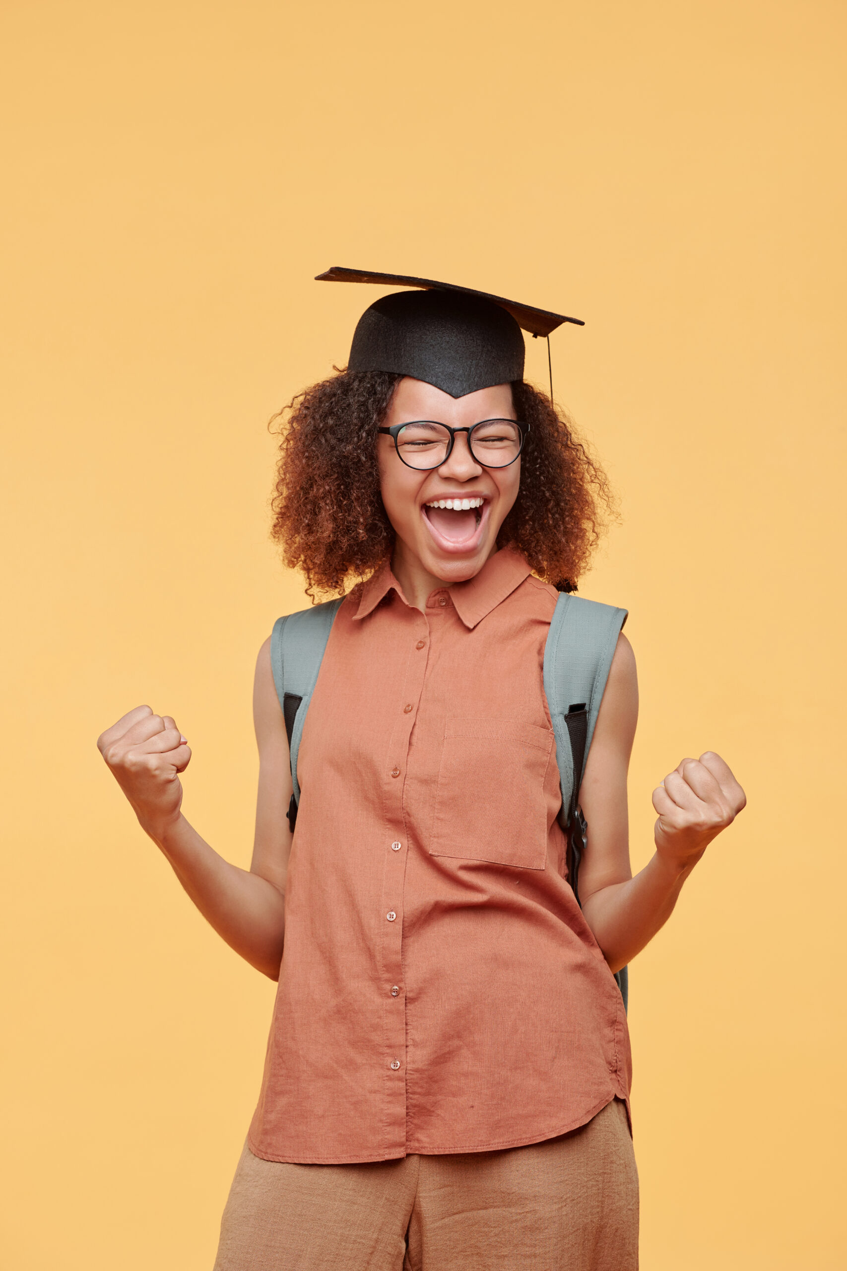 Ecstatic African-American student girl in graduation cap making yes gesture after successfully passed exams